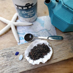 black tea leaves on seashell with tea scoop measure, driftwood, starfish, map and teapot in background