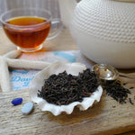 close up of black tea in seashell with beach glass, driftwood, starfish, map and cup with brewed tea and teapot in background