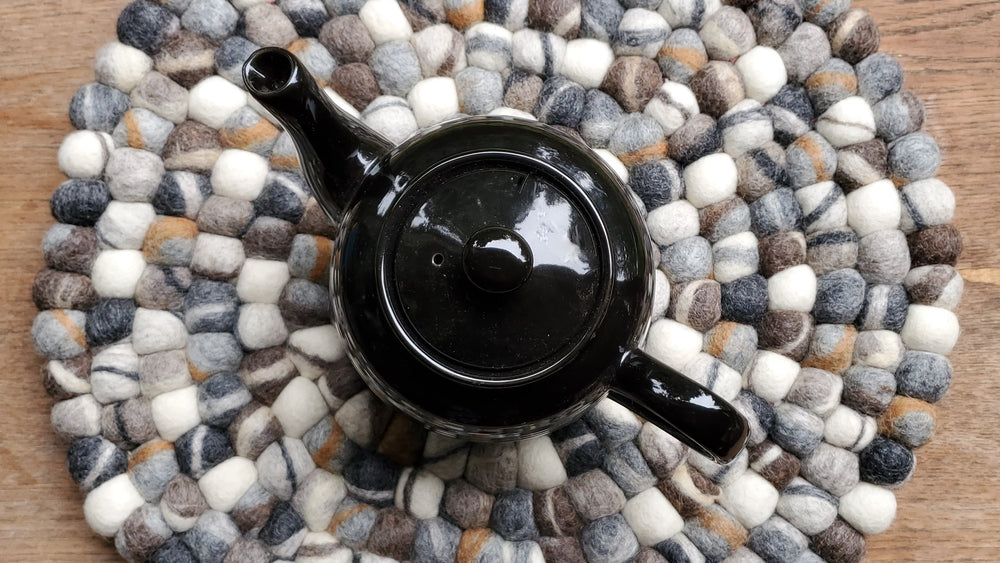 Greytone wood tea trivet with black teapot on wooden table 
