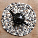 Greytone wood tea trivet with black teapot on wooden table 