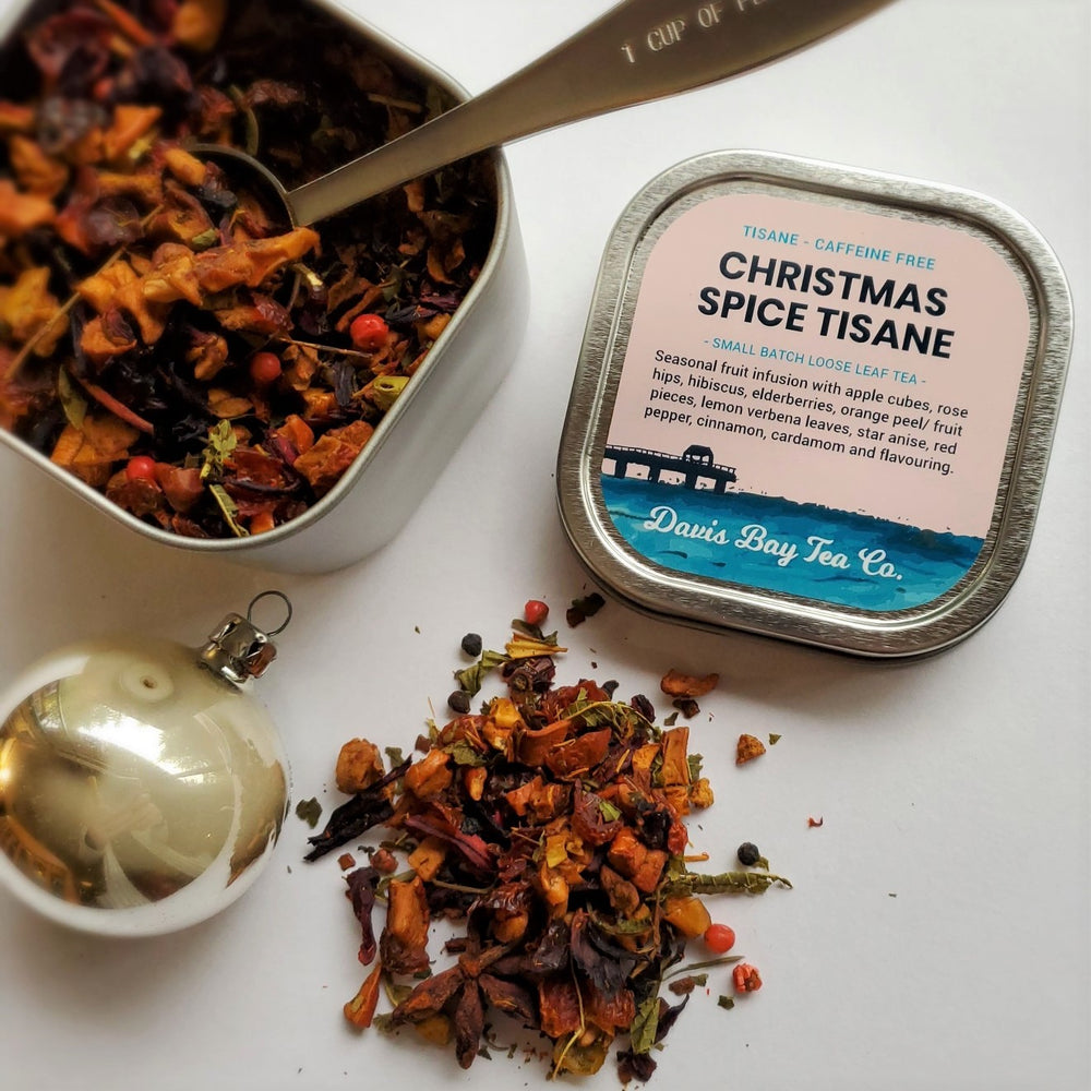 
                  
                    open tin of Christmas Spice Tisane with scoop in tea and pile of tea on display
                  
                