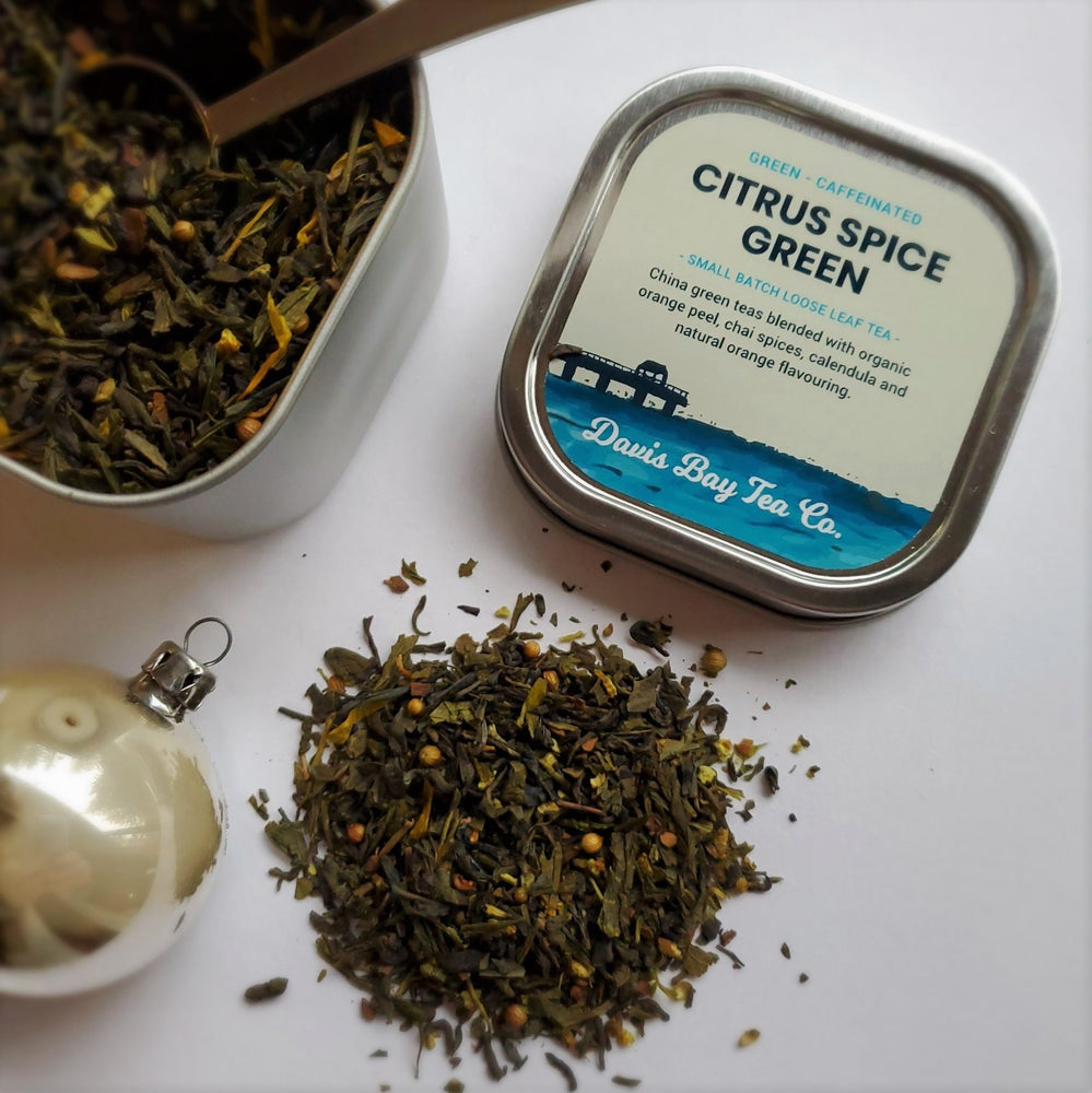 
                  
                    open tin of Citrus Spice Green tea with scoop in tea and pile of tea on display
                  
                