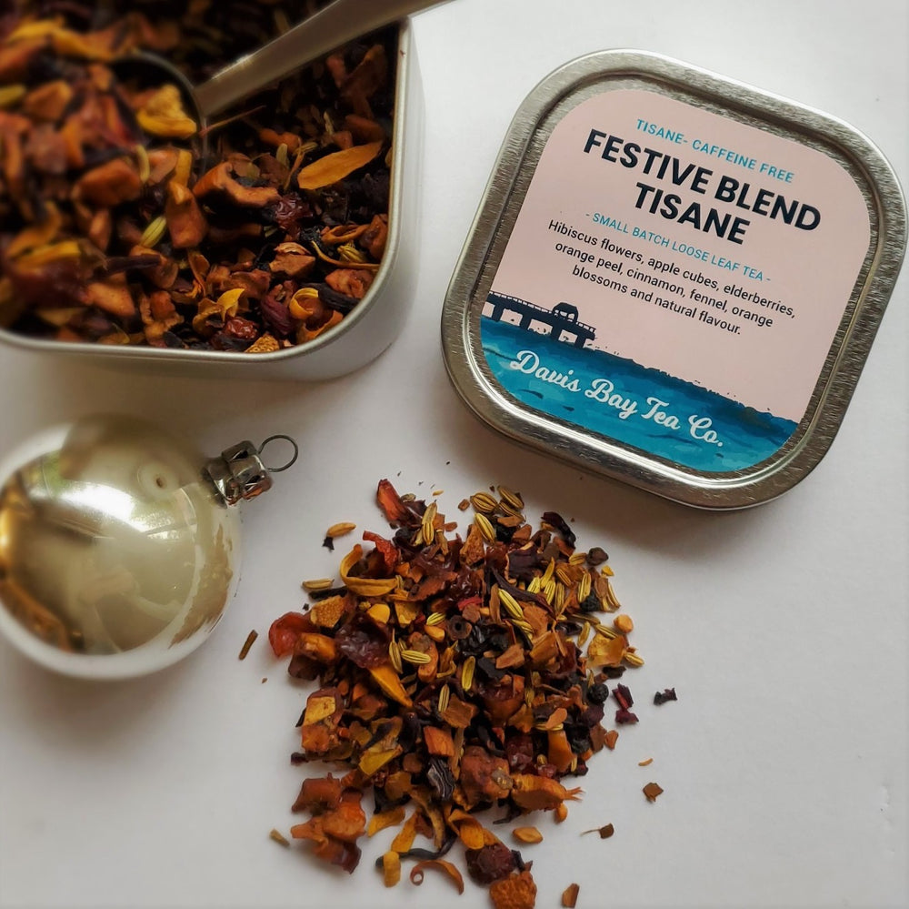 
                  
                    open tin of Festive Blend Tisane with tea scoop and pile of tea on display
                  
                