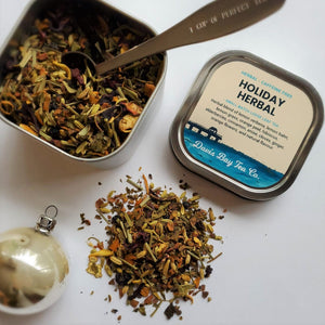 
                  
                    open tin of Holiday Herbal tea with scoop in tea and pile of tea on display
                  
                
