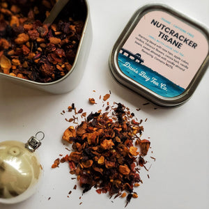 
                  
                    open tin of Nutcracker Tisane with scoop in tea and pile of tea on display
                  
                